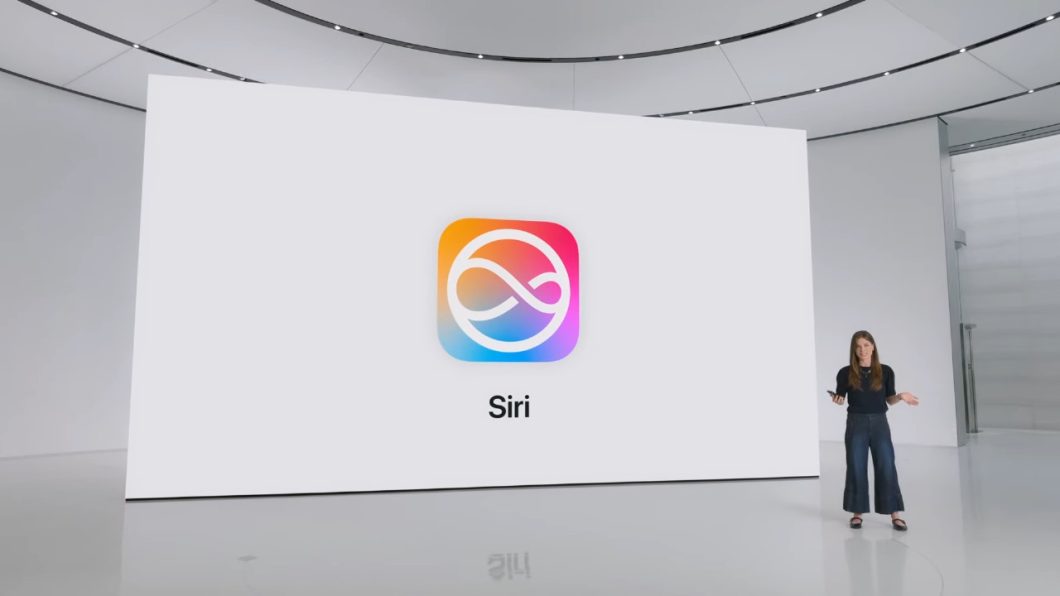 Imagem de uma mulher em um palco virtual. Atrás dela, uma tela gigante com um logo colorido da Siri.
