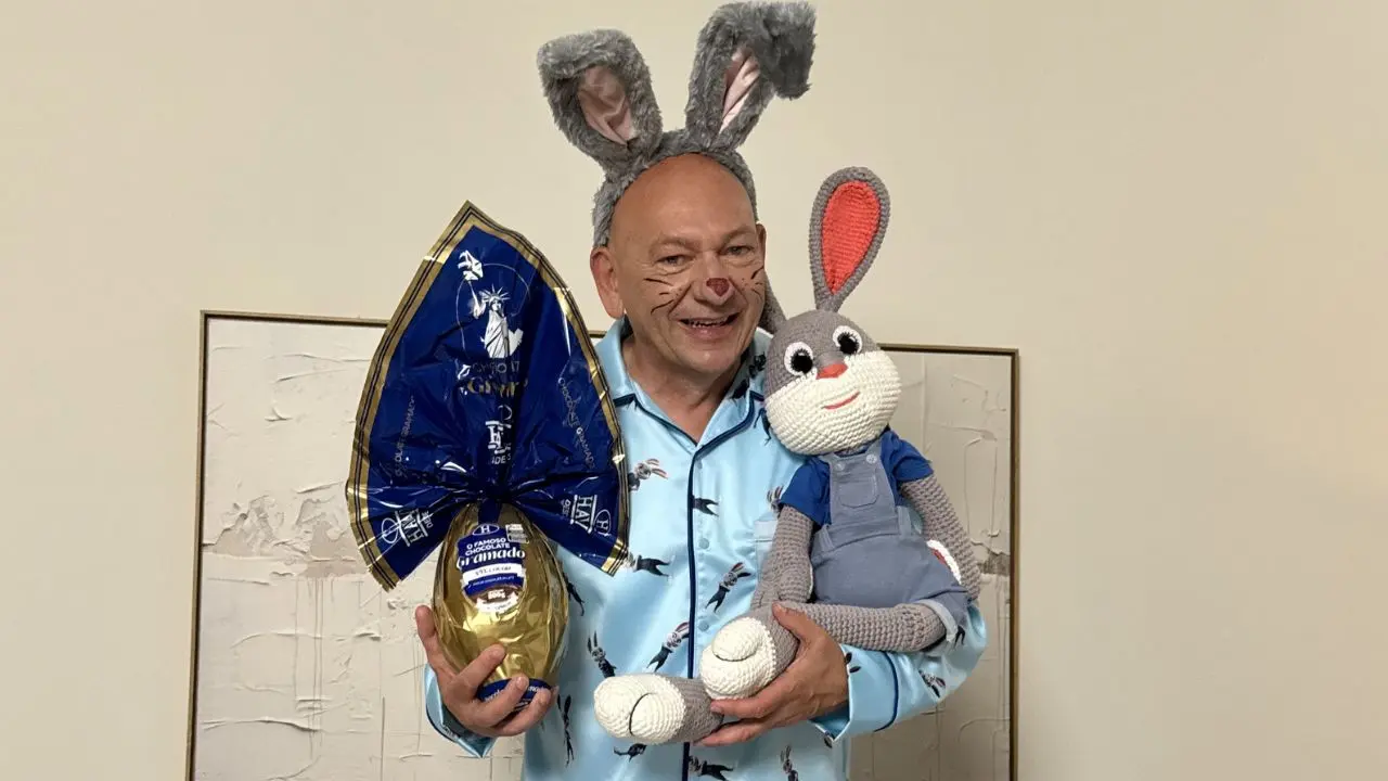 empresário dono da Havan, Luciano Hang, vestido com um pijama azul, com orelhas e maquiagem de coelho da Páscoa, segurando em uma das mãos um coelho de pelúcia e na outra um ovo de páscoa