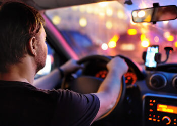 Motorista masculino dirige um carro durante o engarrafamento da noite. Vista interior.
