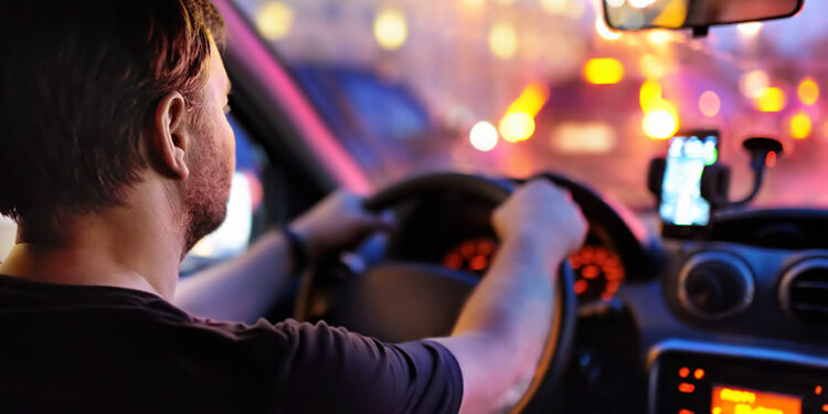 Motorista masculino dirige um carro durante o engarrafamento da noite. Vista interior.